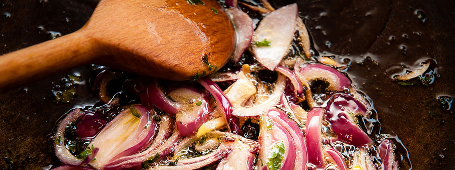 Close up of red onions frying in oil, in a pan with a wooden spoon